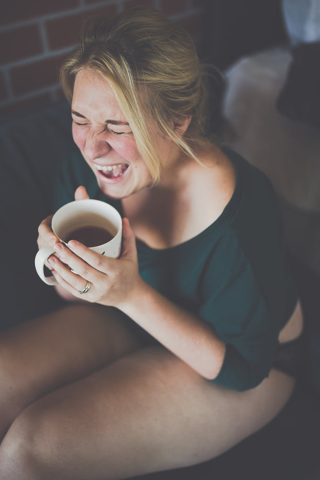 Evie Mitchell a white author with blonde hair is holding a cup of tea and laughing